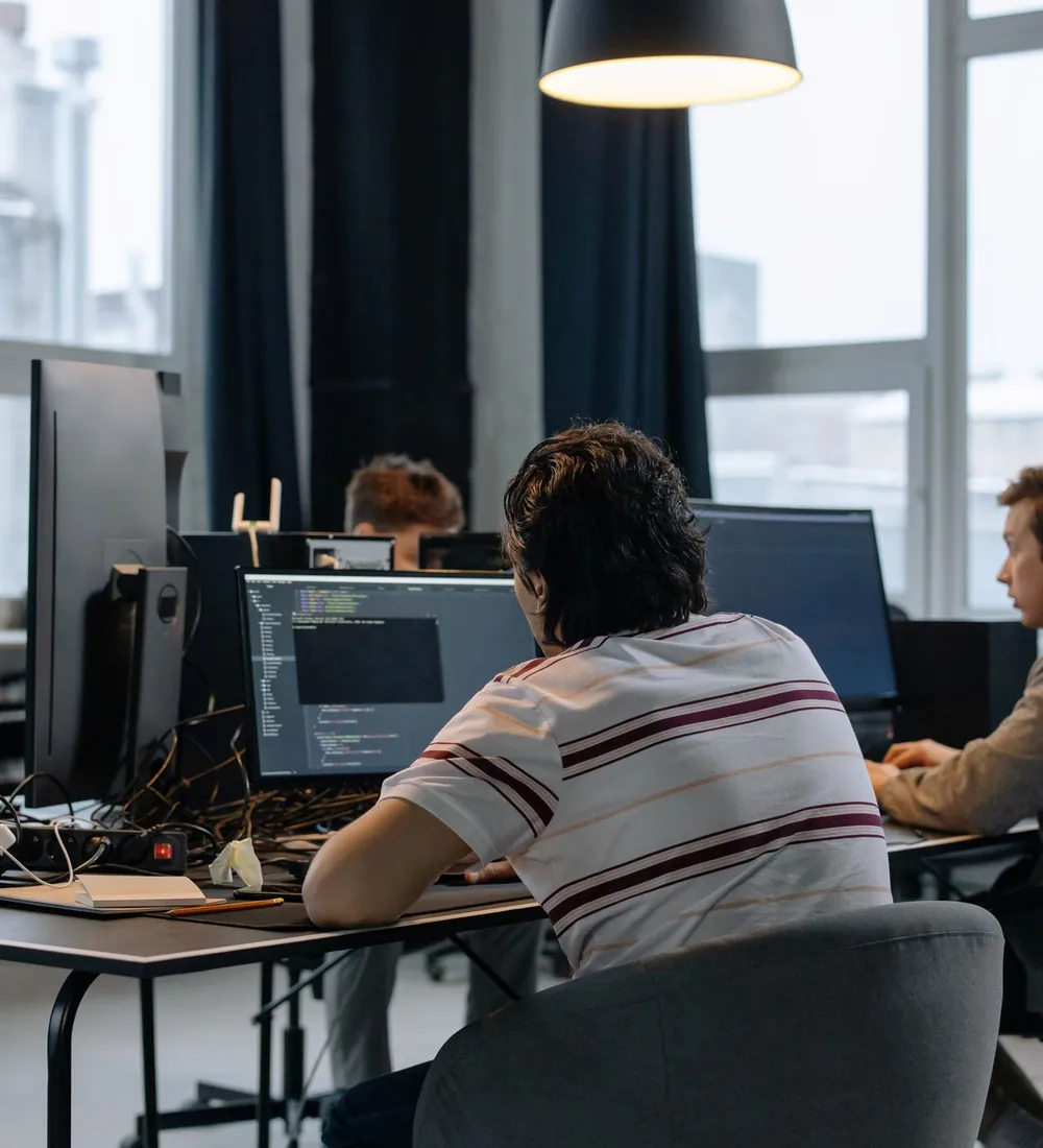 An engineer at a desk with two monitors, in a shared office.
